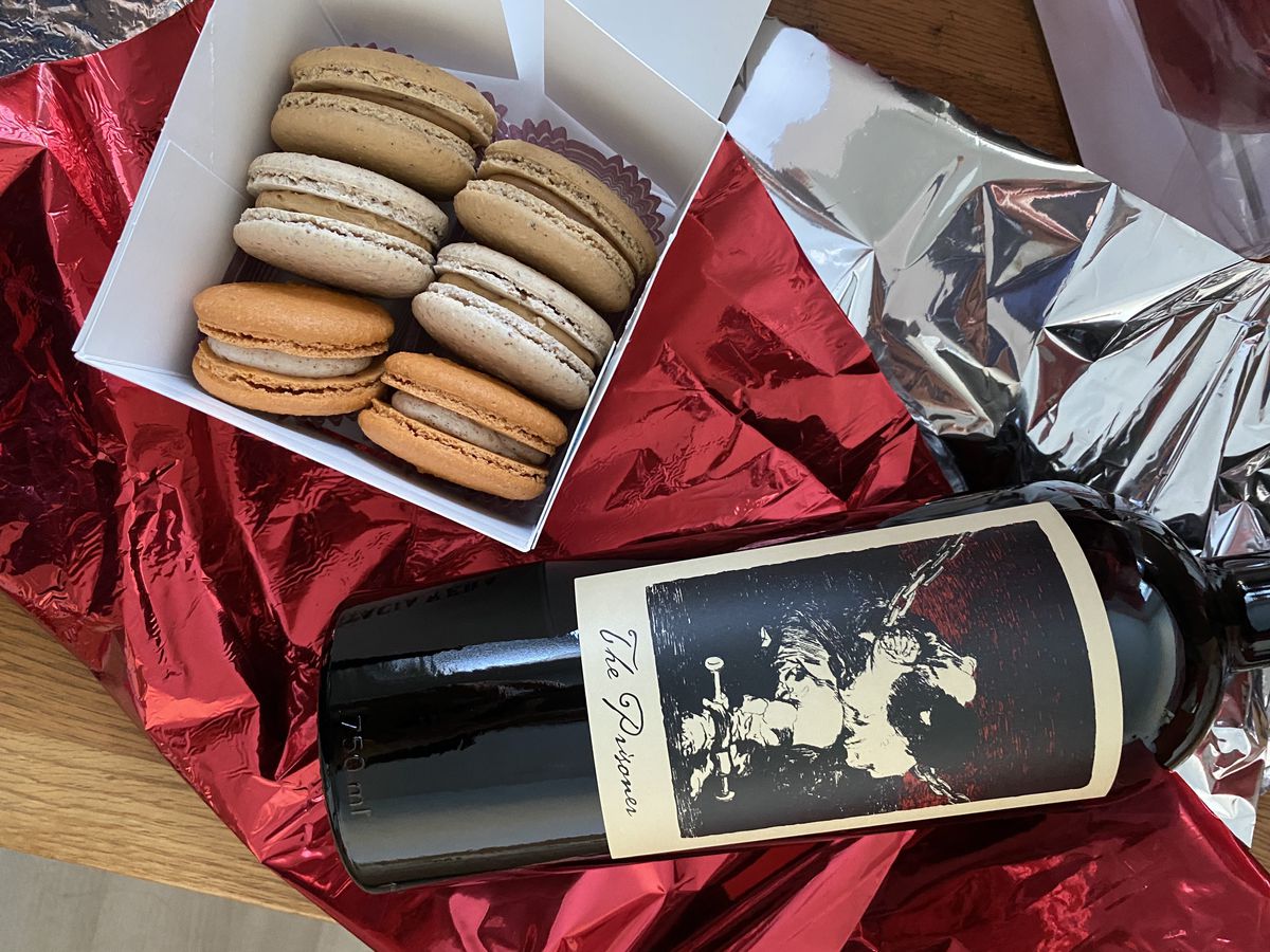 From above, a paper box of macarons in various shades, alongside a large bottle of red wine