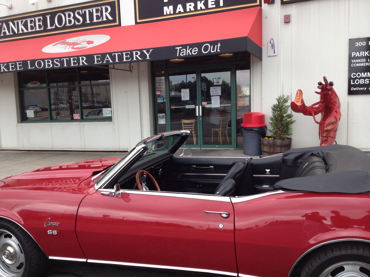 A red convertible with the top down parked outside of a restaurant with a red awning.