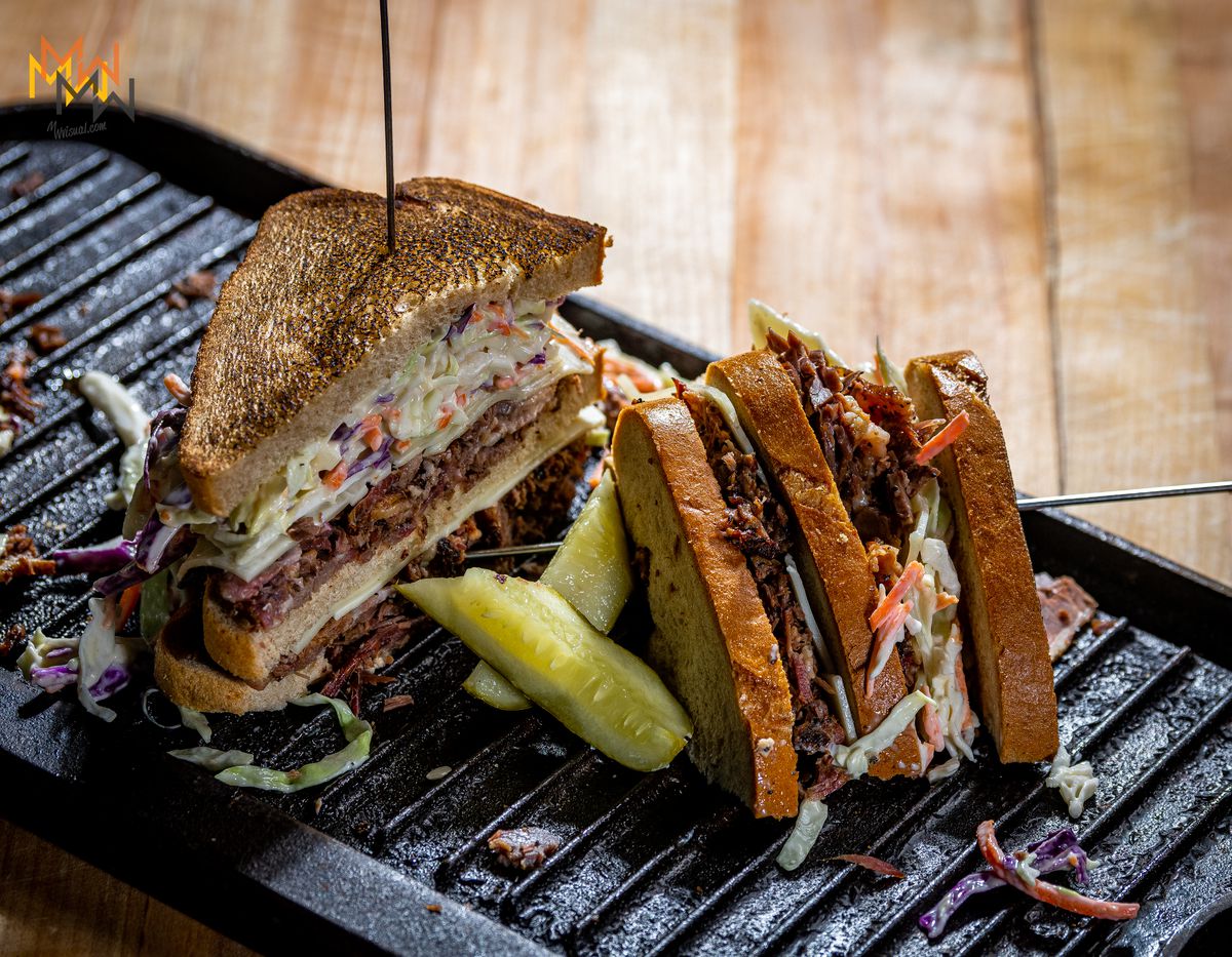 a pastrami sandwich, sliced in half, on a grill.