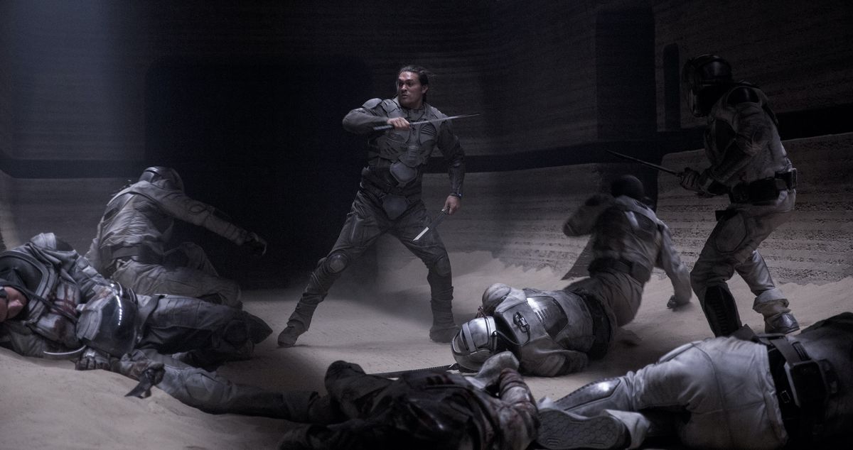 Jason Momoa as Duncan Idaho, wielding two blades and surrounded by collapsed or collapsing soldiers in grey armor in Dune