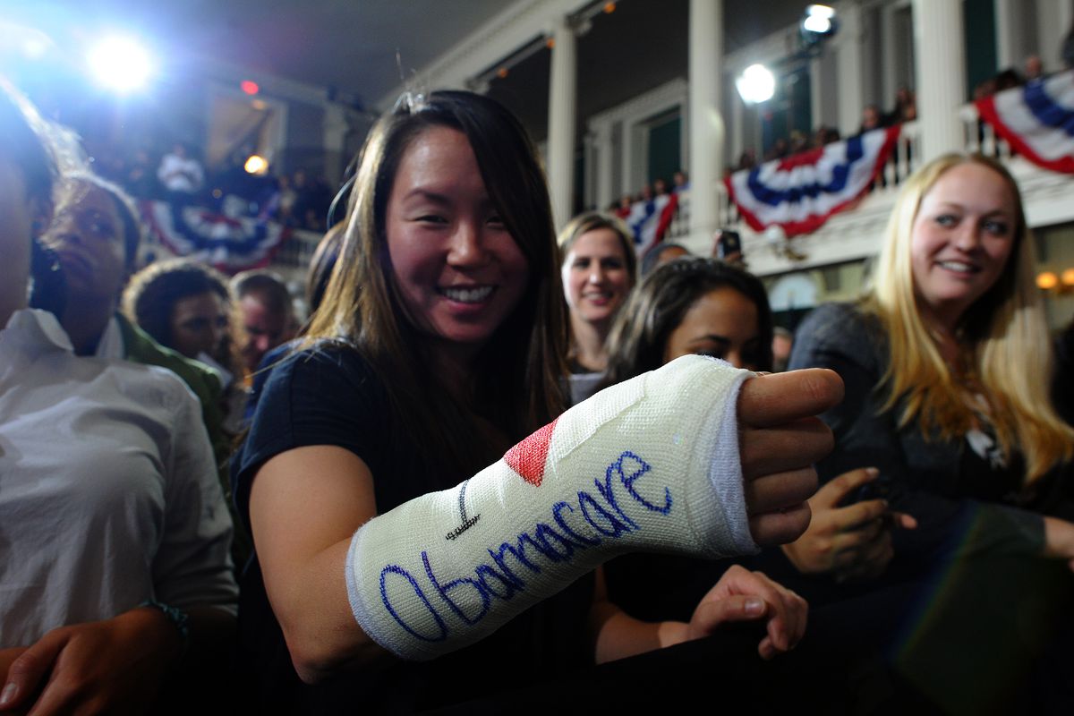 Woman holds up a cast with words "I 'heart' Obamacare"