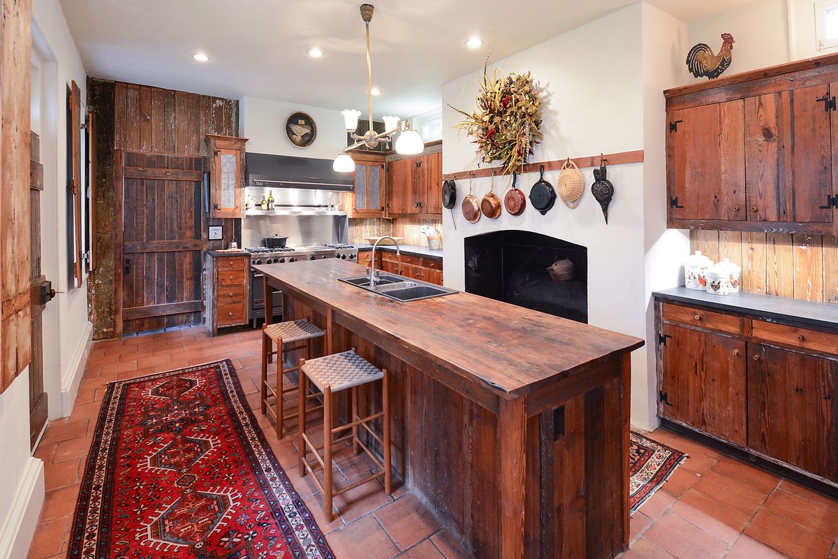 A rustic kitchen with a large wooden island, red tile floors, and a fireplace. 
