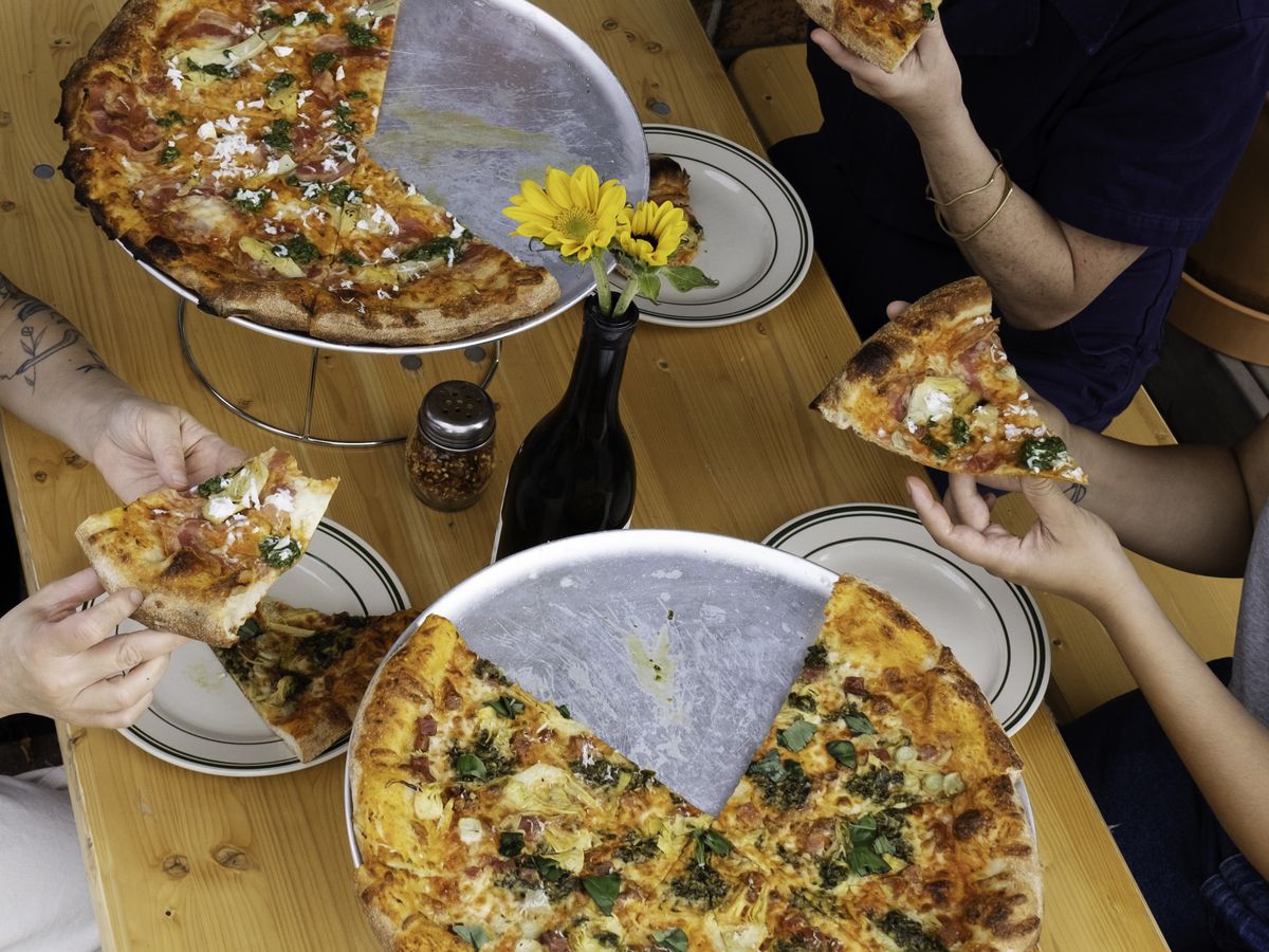 Diners dig into two pizzas with toppings.