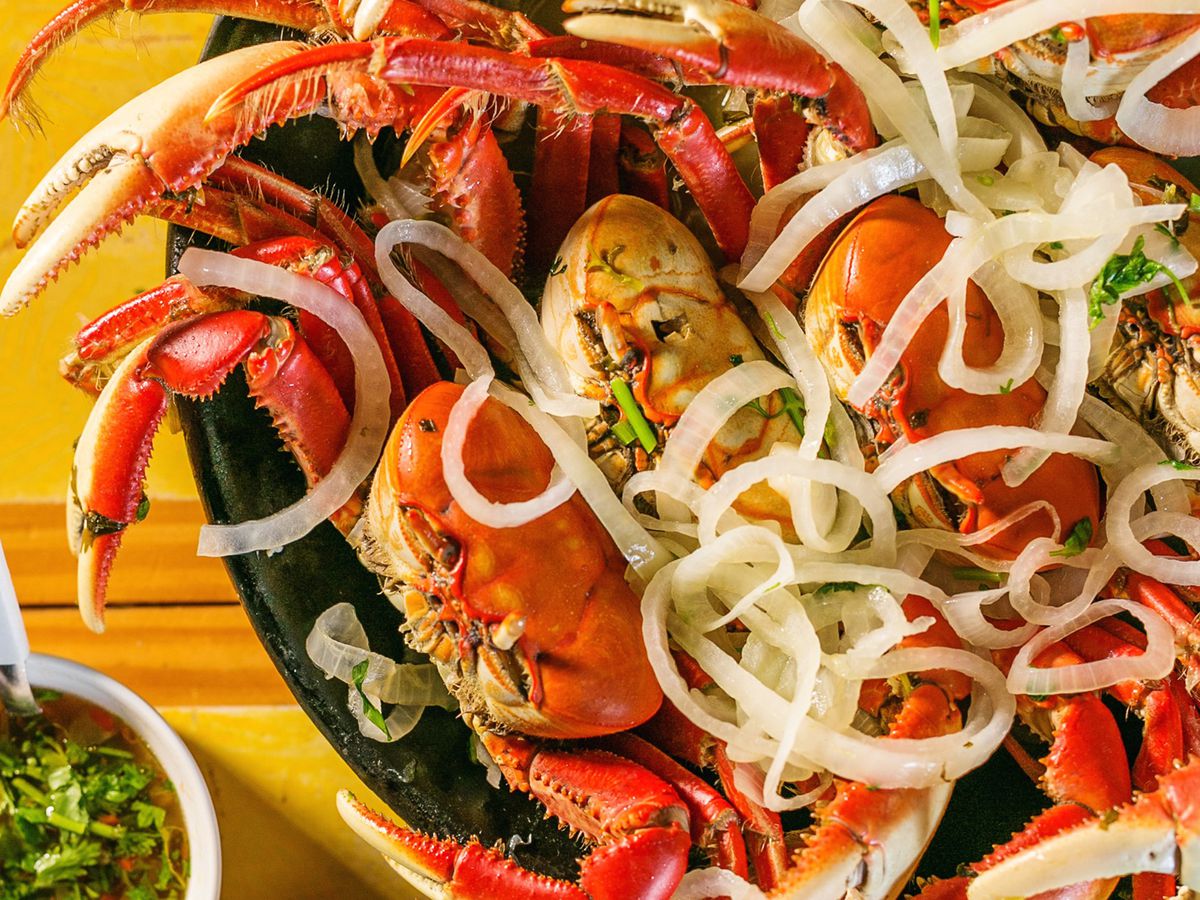 Bright red whole crabs served beneath a layer of grilled onions, with other dishes on the side