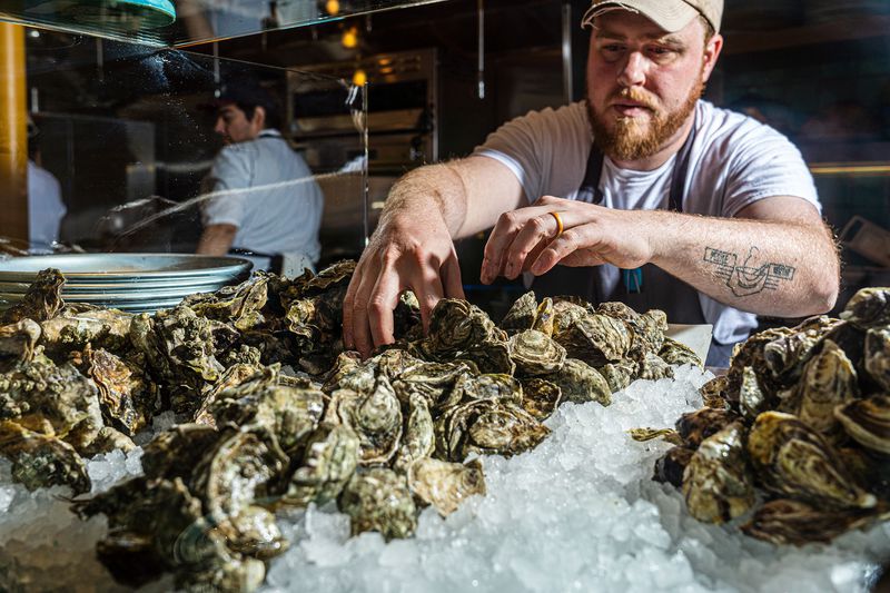 A pair of hands reaches into a pile of unshucked oysters on ice. 