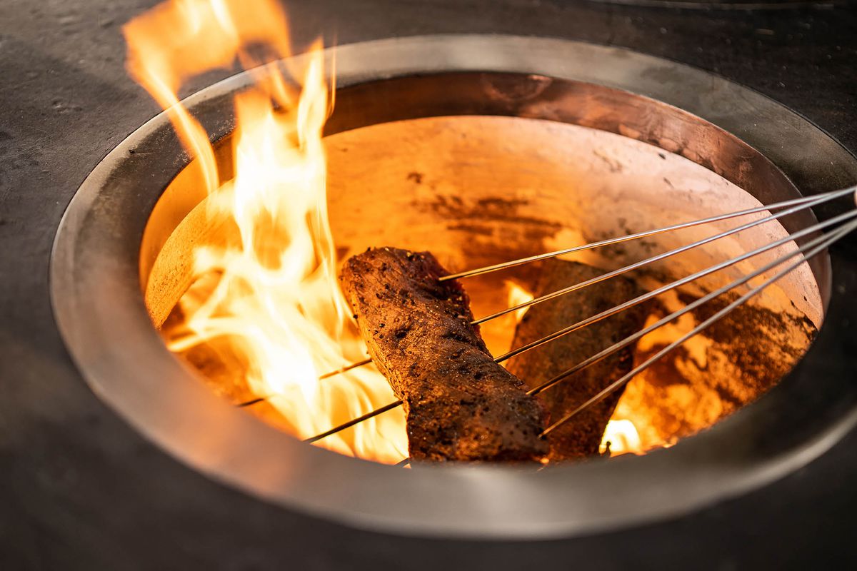 Metal skewers inside of a piece of meat as it sits over an open flame at a restaurant.