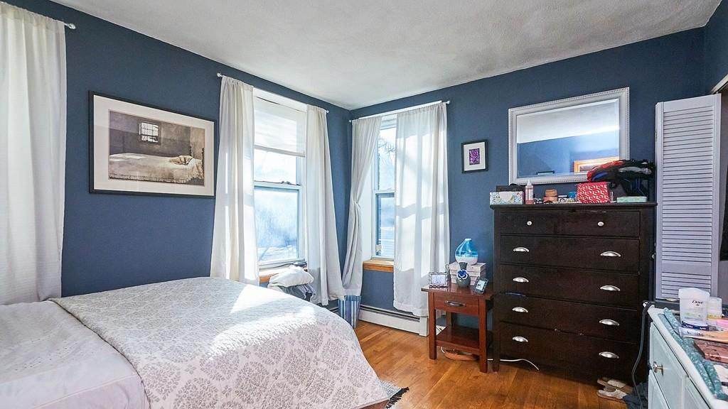 A bedroom with a bed facing a dresser, and there are two windows. 