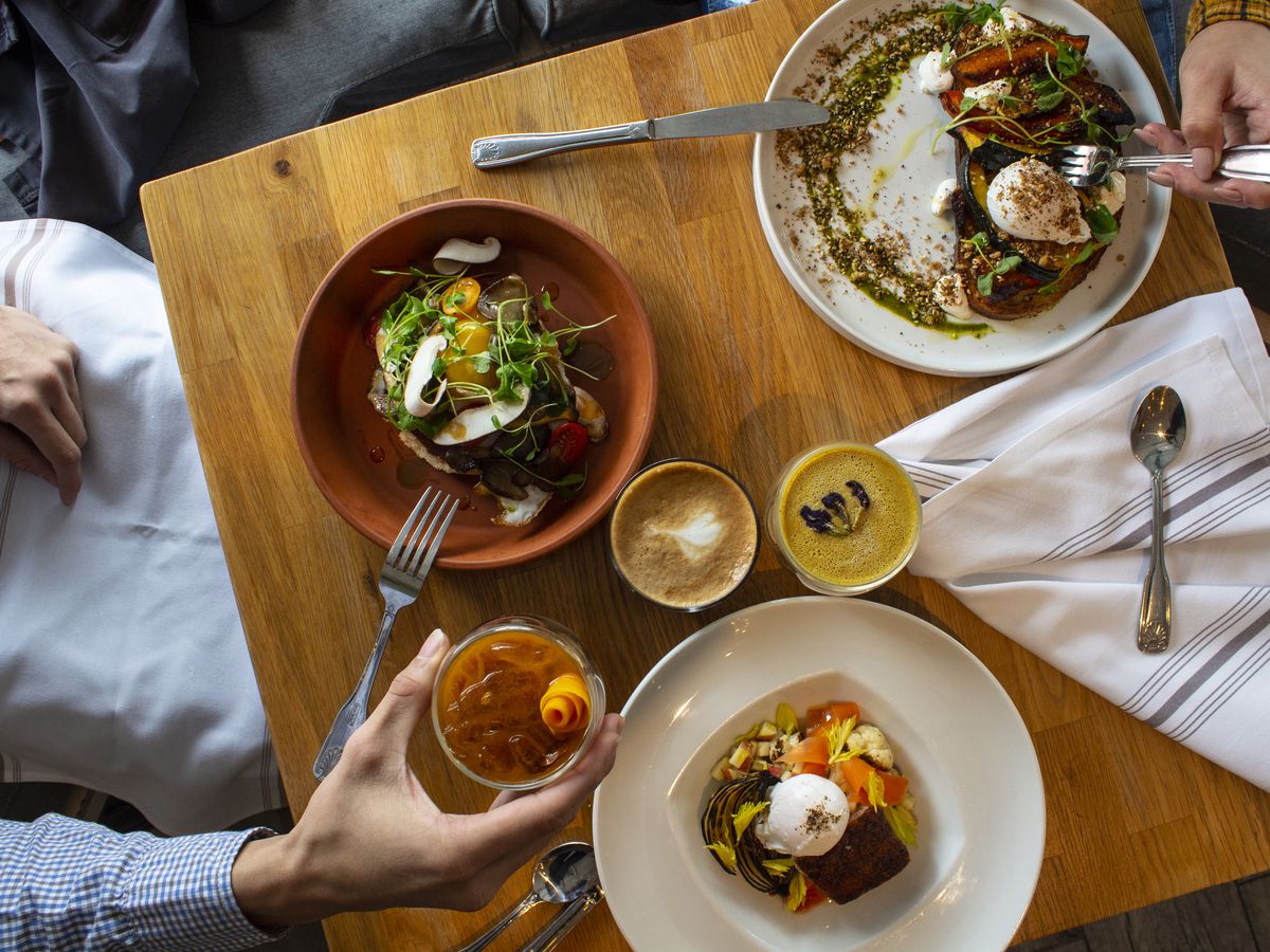 An aerial shot of two people sitting at a table with three dinner dishes, a coffee, turmeric latte, and iced beverage. 