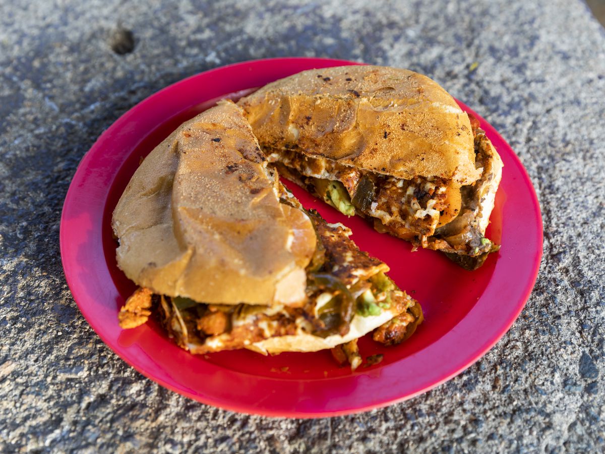 An overflowing torta, split in half, on a red plastic plate on concrete surface