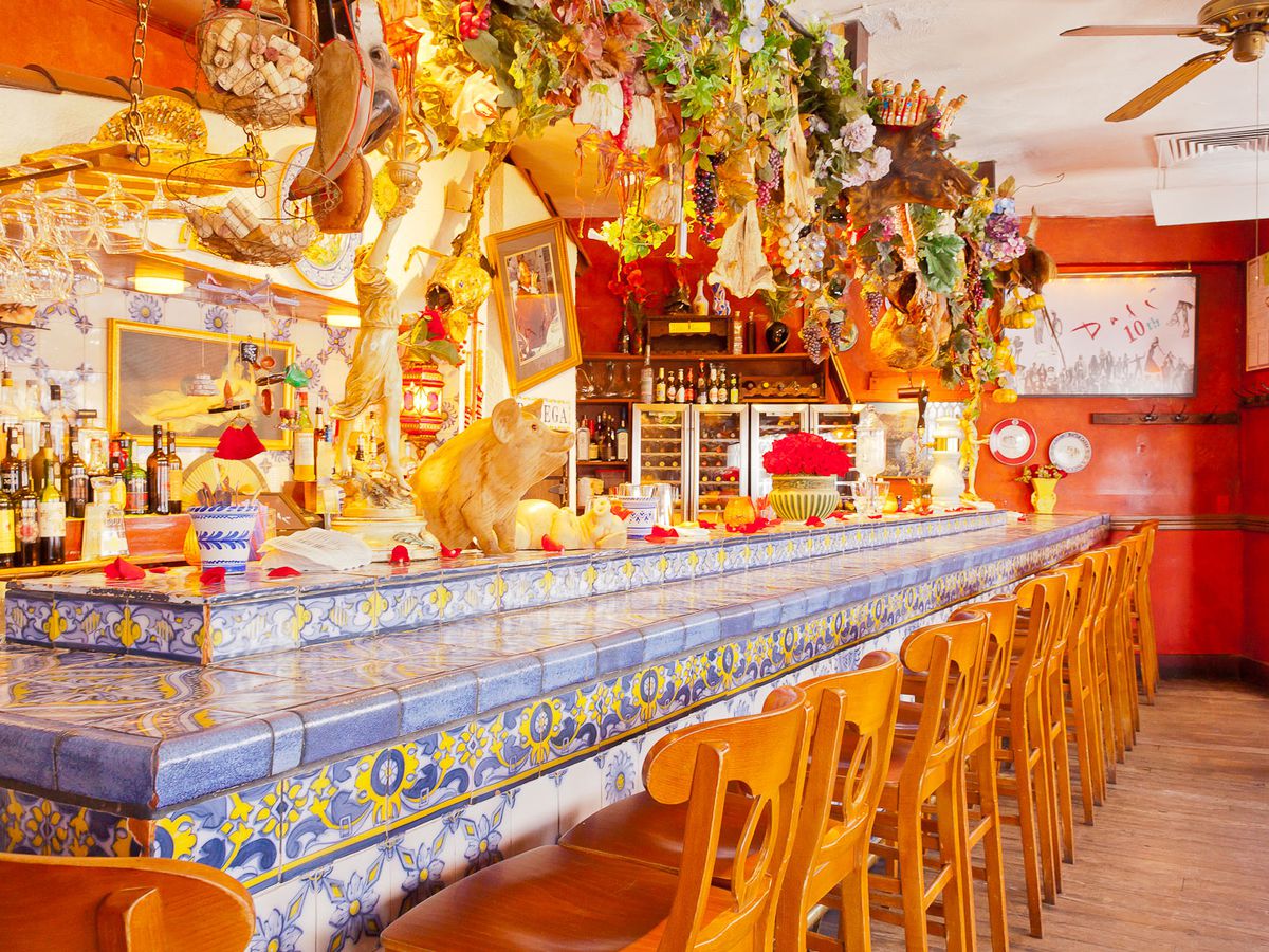 An intricately decorated restaurant bar features blue and yellow Spanish tiling and lots of decorative dried flowers hanging above.