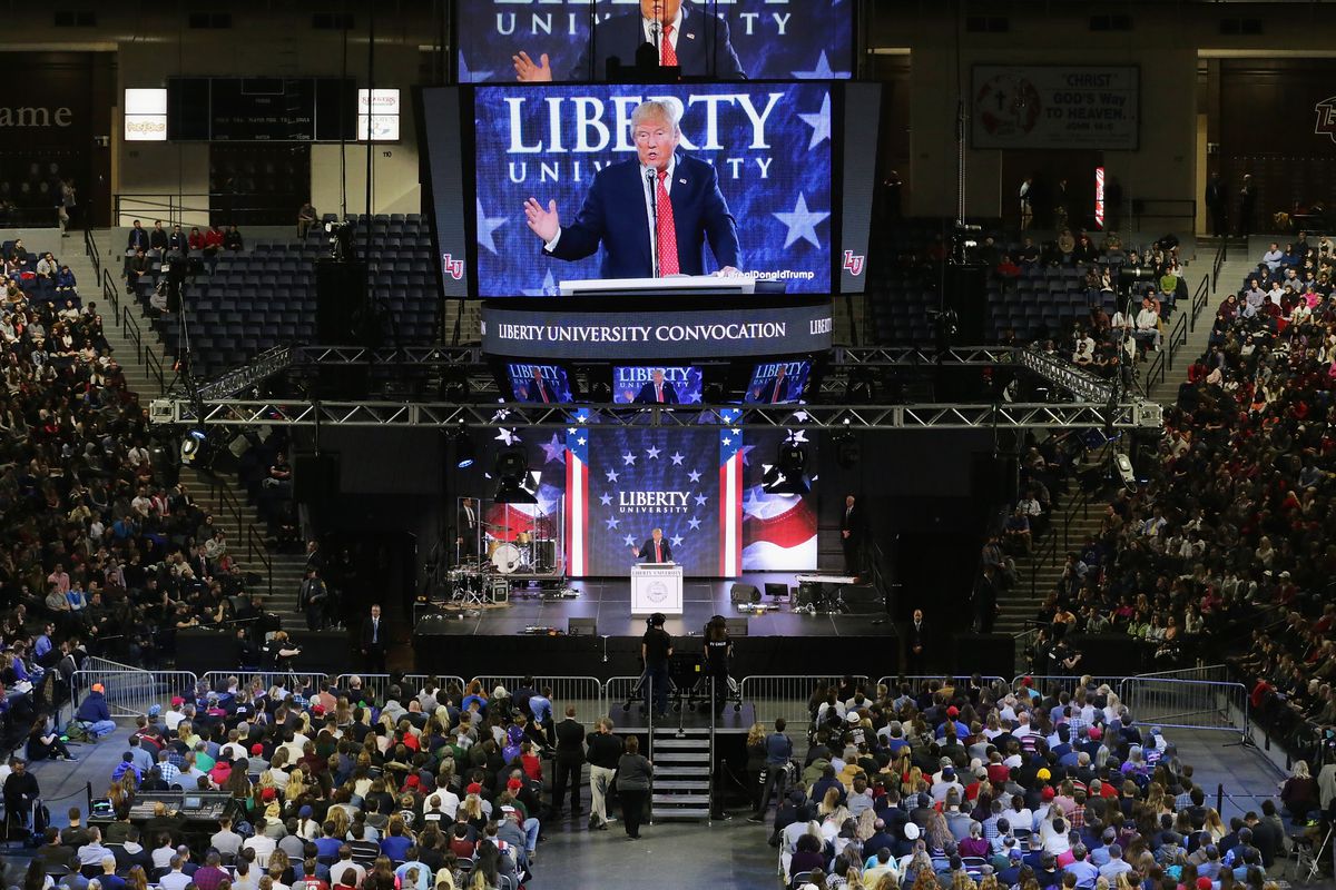Donald Trump, speaking in a large campus center at Liberty University, with a large screen behind him projecting his image.