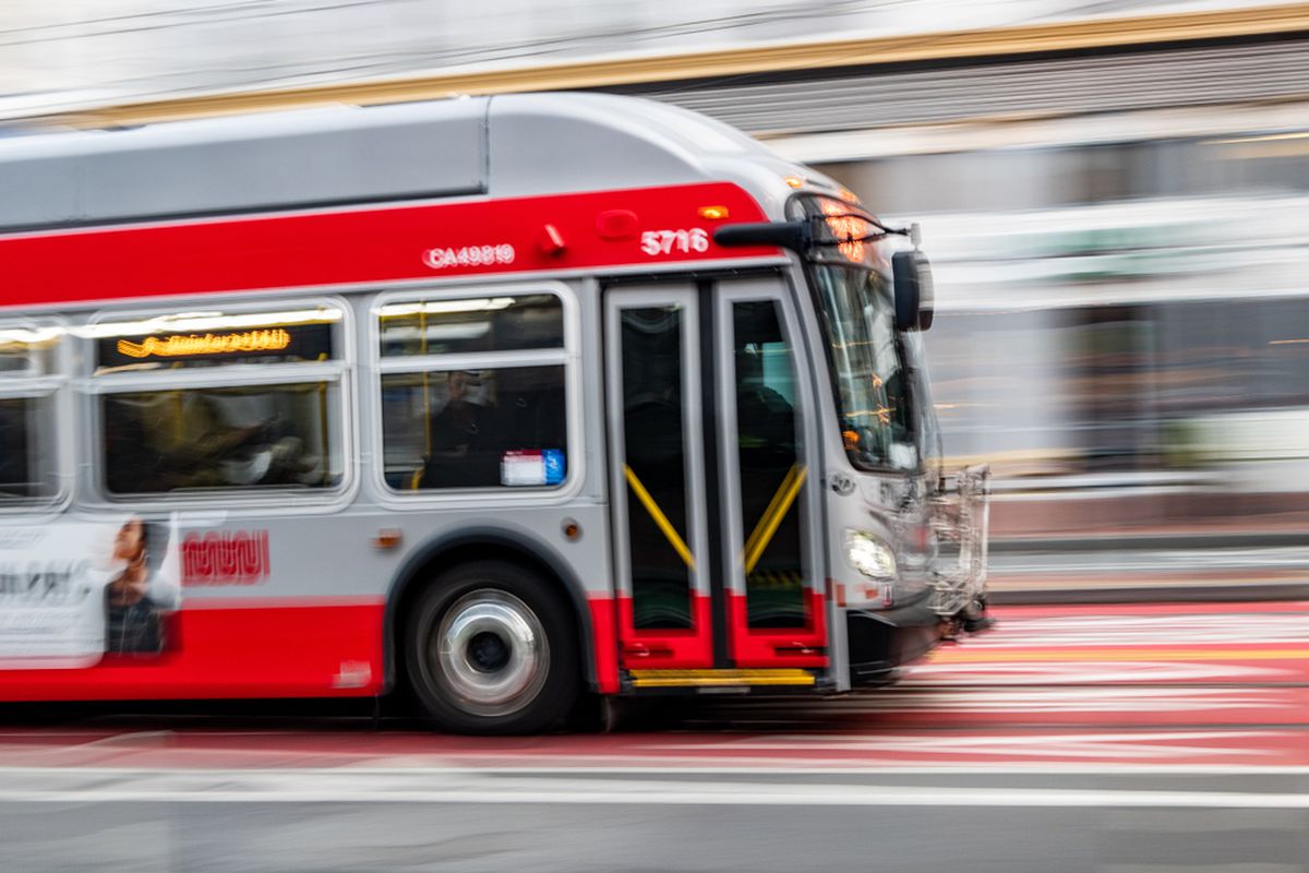 Two red and gray buses passing each other, one of them a blur.