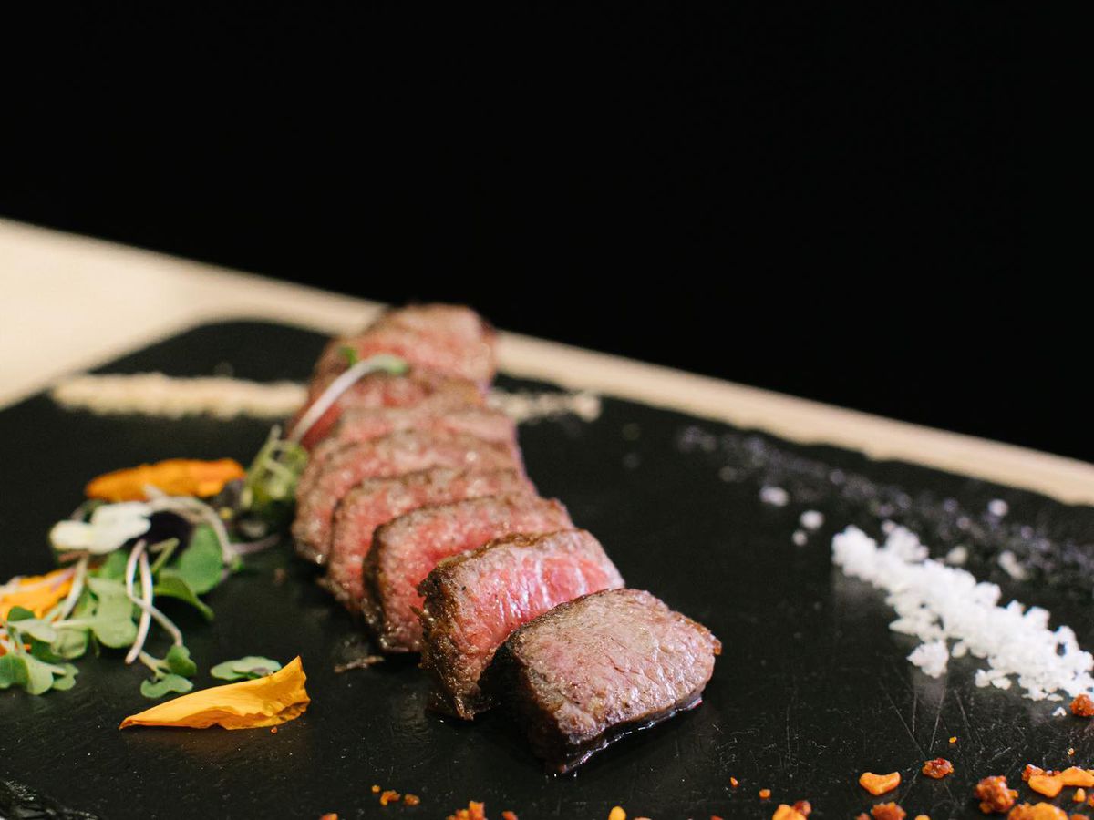 Pieces of wagyu steak on a black plate with salt and chile flakes on the side.