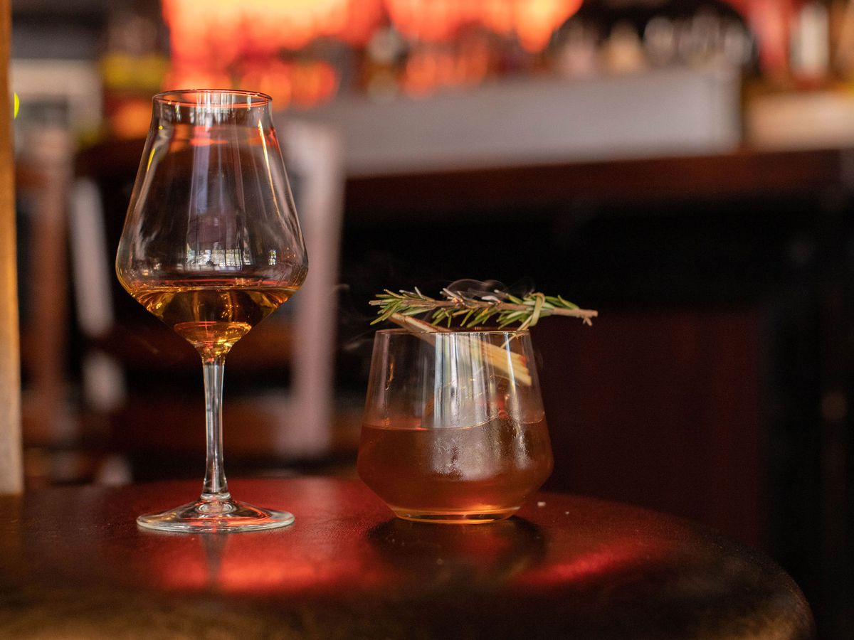A glass of Highland Park whisky neat next to a cocktail garnished with a rosemary spring.