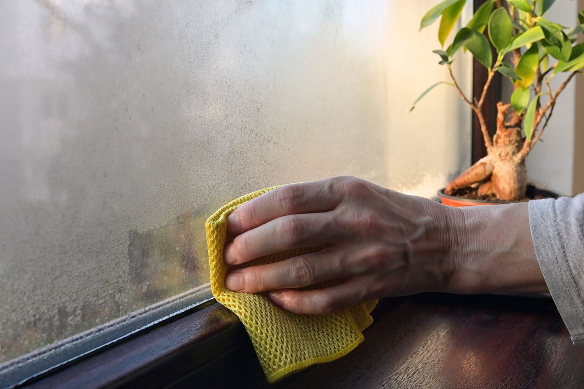 A hand wiping down a window with condensation.