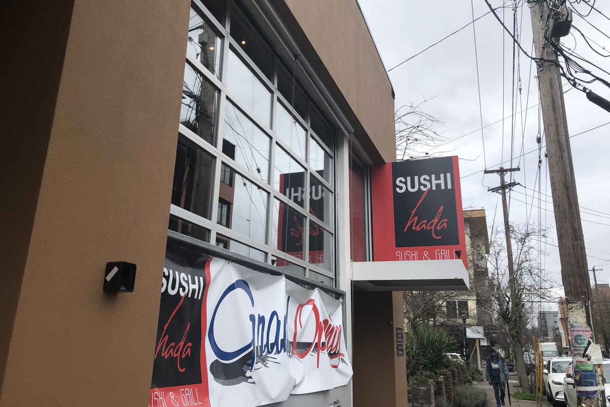 A picture of a sign that reads “Sushi Hada,” a restaurant lined with garage-style windows