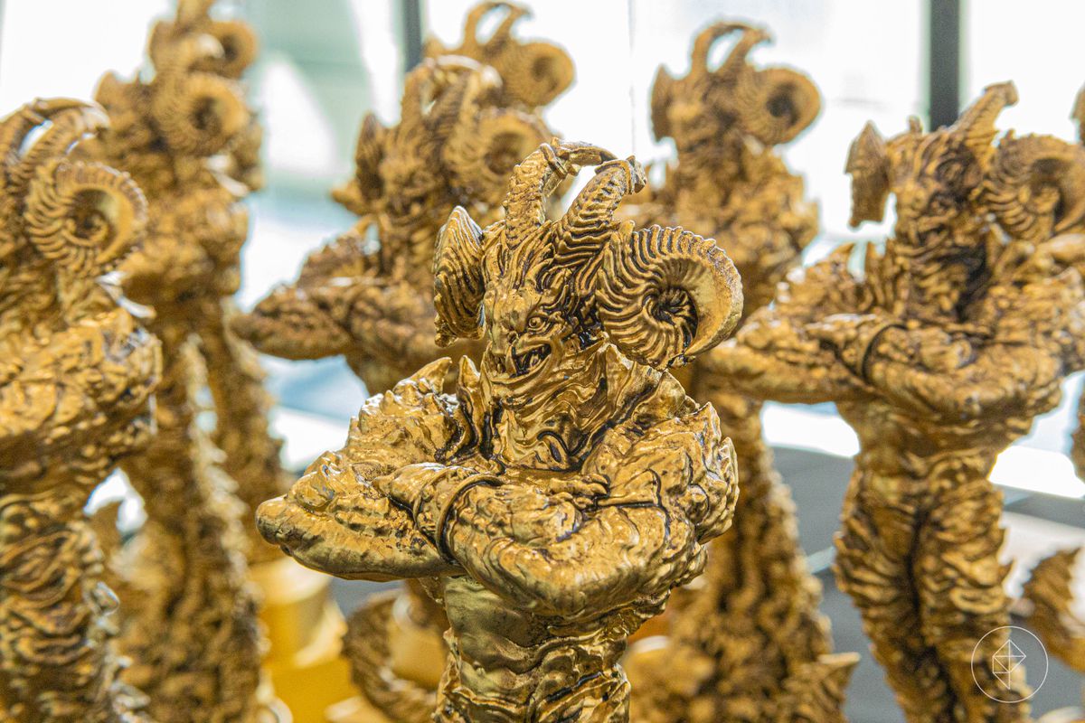 A Golden Demon award standing next to a dozen examples. Its arms are crossed, its face locked in a rigid grin.