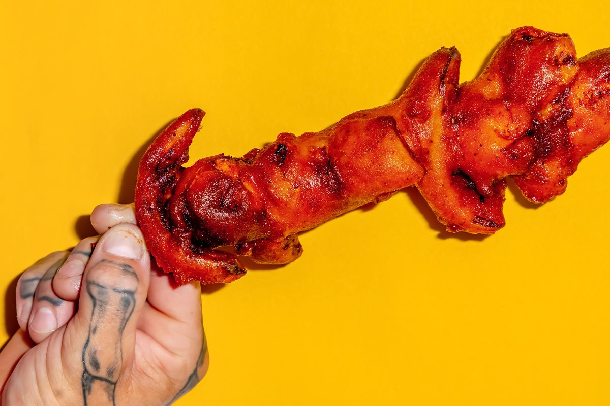 A hand holding Cajun chicken on a stick against a yellow background