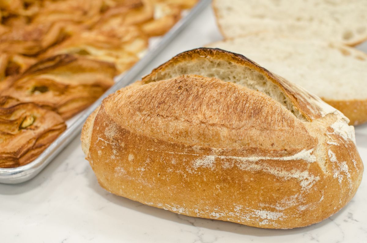 One big sourdough loaf is in the foreground of the picture, with a sliced loaf visible in the background. Some flaky puff pastries are off to the side.