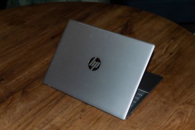 The HP Pavilion Plus half open, seen from the back on a wooden table.