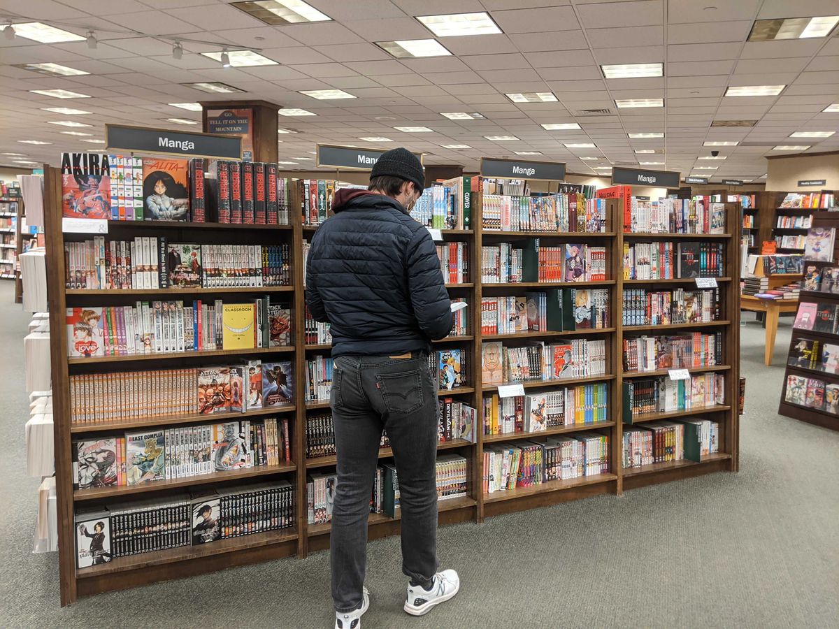 Un joven de pie hojeando algunos manga en la sección de manga de Barnes and Noble