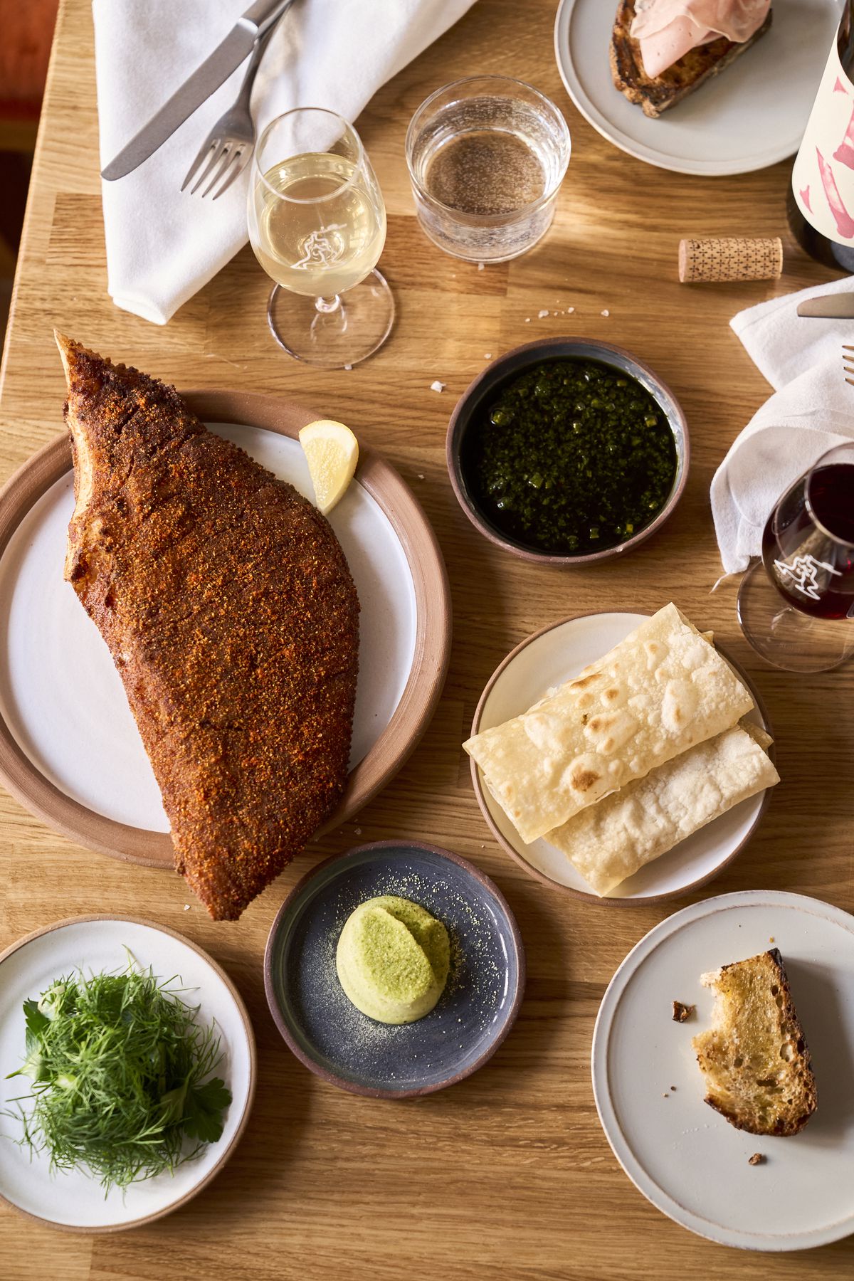 An overhead photograph of a fried skate wing and other dishes at Place des Fêtes, a wine bar in Clinton Hill, Brooklyn.