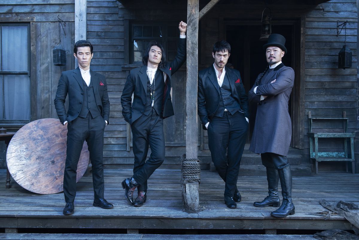 Jason Tobin, Chen Tang, Andrew Koji, and Hoon Lee look cool as shit while leaning on a wooden post in Warrior. Tobin, Tang, and Koji wear black suits with a red handkerchief, while Lee wears a top hate and a grey suit.