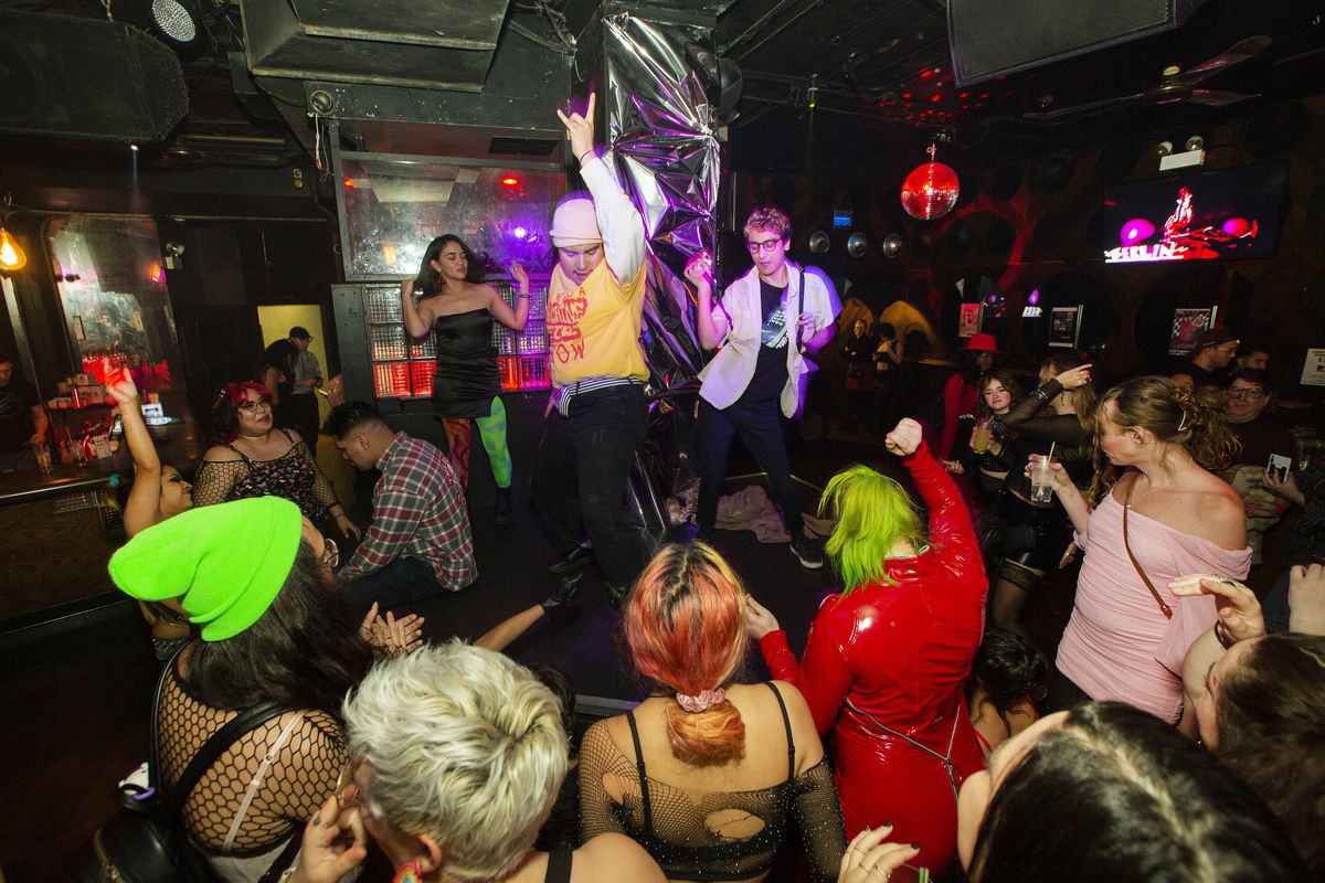 Three people dance on a stage inside Berlin nightclub. A crowd surrounds them on the floor, also dancing.