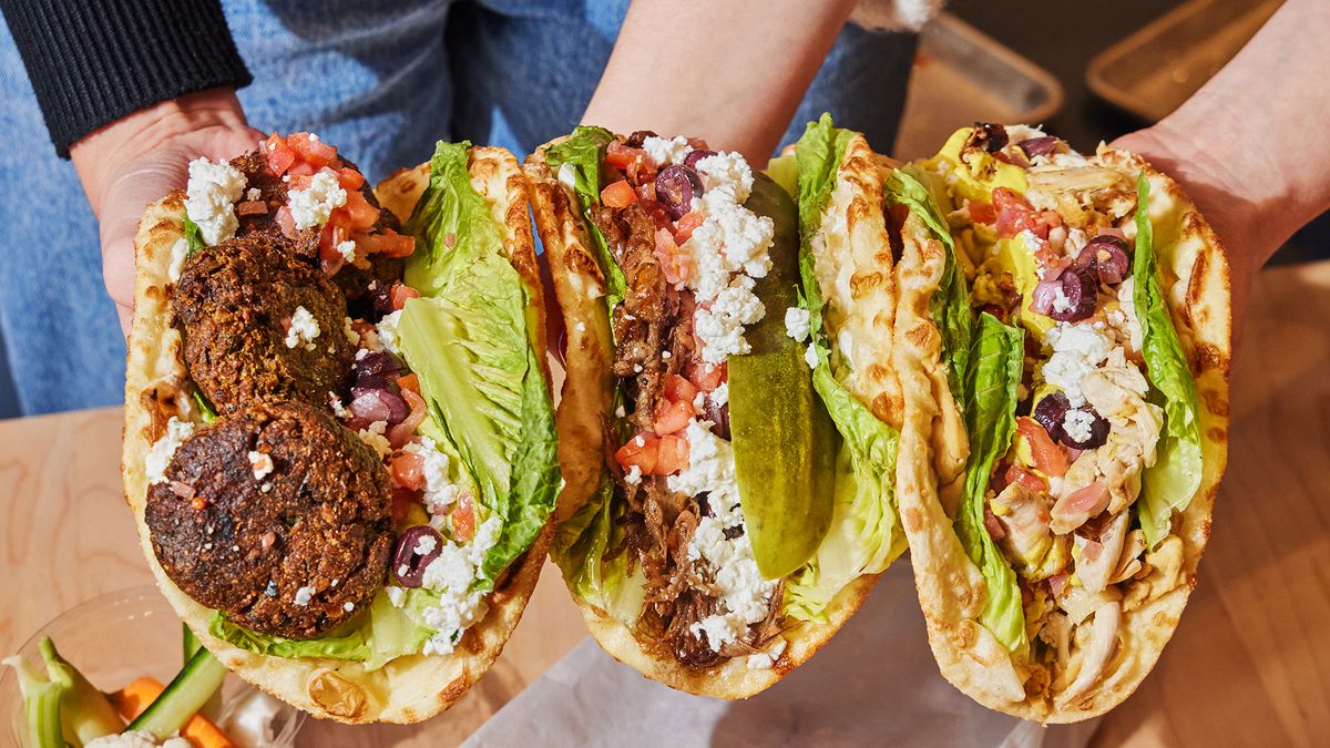 Three pita sandwiches held up and faced to the camera to reveal fillings including falafel, cheese, and lettuces.