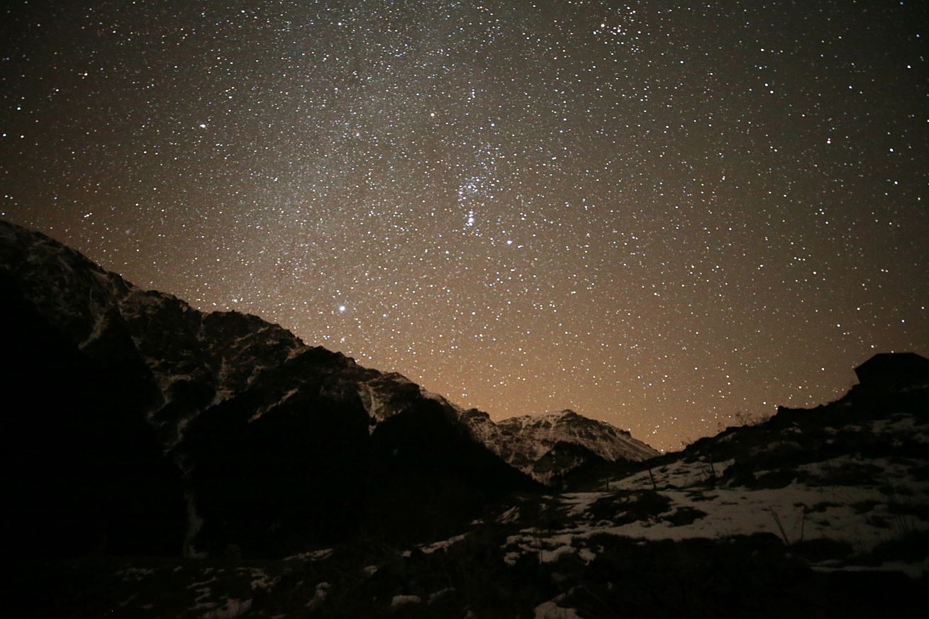 Stars shine brightly in the night sky over a snowy mountain range.