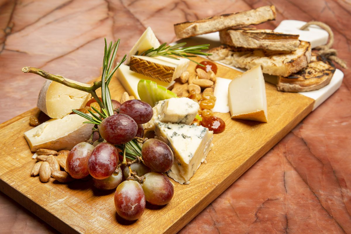 A wooden cheese board laid with hunks of cheese and a cluster of red grapes.