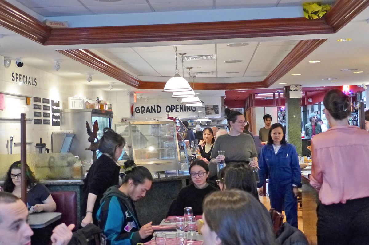 A crowded room of customers, with Grand Opening on a banner at the rear.