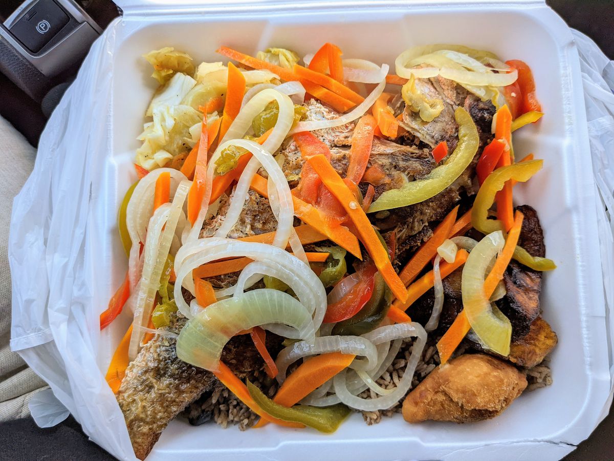 An open Styrofoam to-go box shows snapper escovitch topped with red peppers, onions, and cabbage at Country Style Jamaican Restaurant.