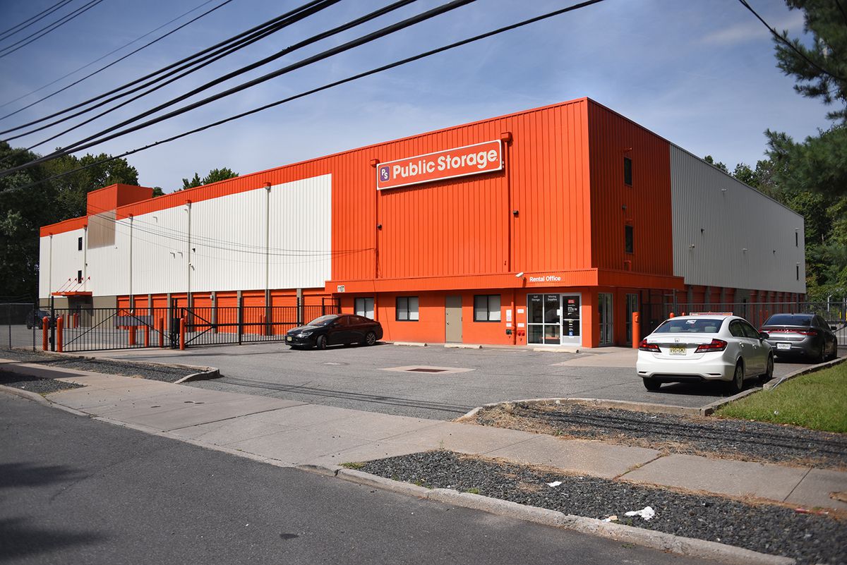 An orange and white building with a sign that says “Public Storage” on it. Three cars are in the parking lot for the building. 