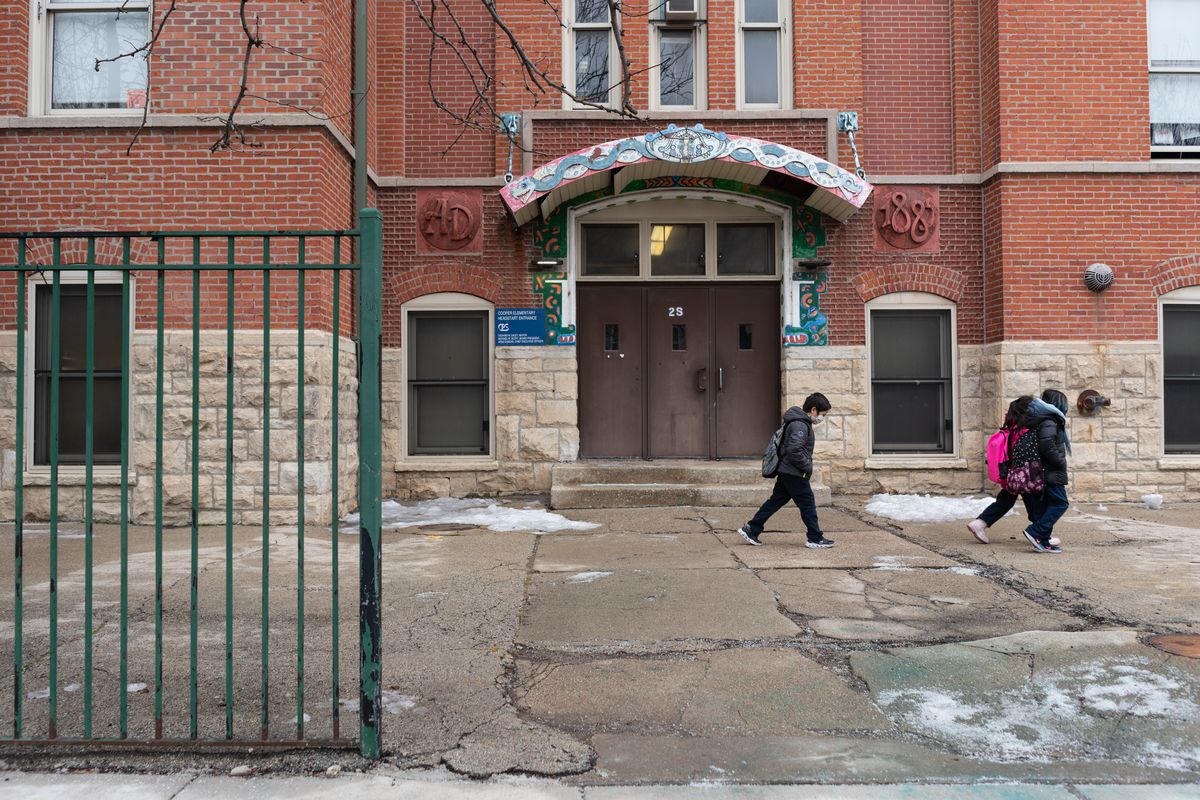 Three young students walk past a doorway at Cooper Dual Language Academy, all wearing winter clothing.
