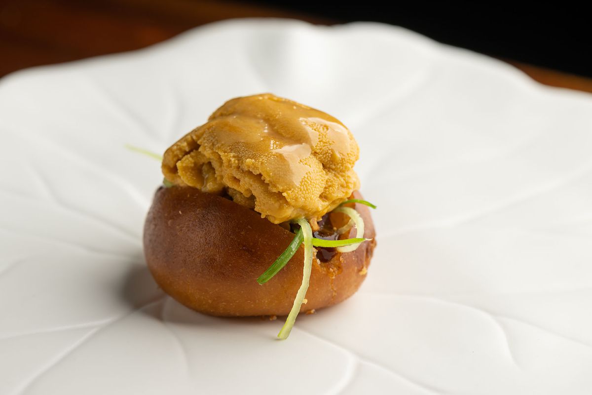 Uni on a browned bun with scallions on a white ceramic leaf looking plate.