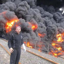 This Wednesday, Feb. 15, 2012 file image provided by the Local Coordination Committees in Syria which has been authenticated based on its contents and other AP reporting, shows anti-Syrian regime activist Khaled Abu-Salah stands in front of flames and black smoke from a bombed oil pipeline, in Baba Amr neighborhood in Homs province, central Syria. 