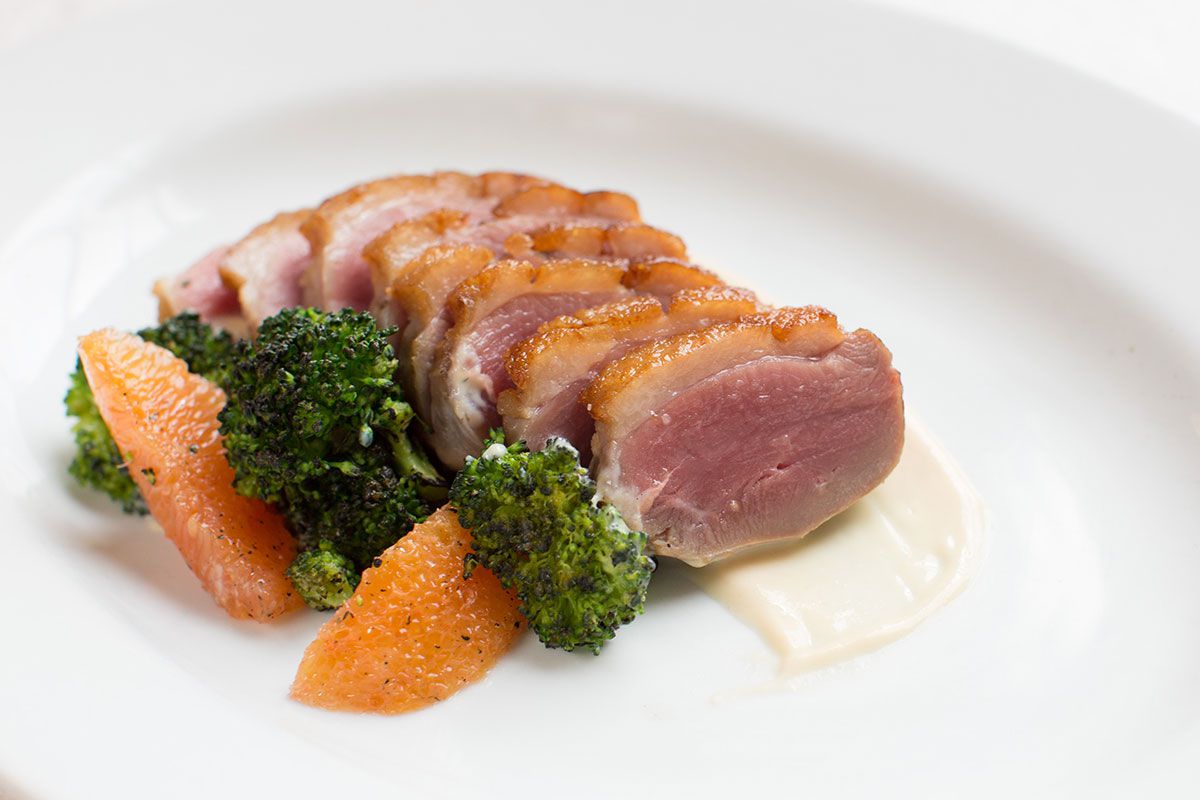 Sliced duck breast cooked rare with broccoli and orange wedges. 