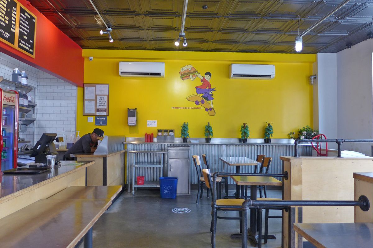 A yellow wall with a mural of a skateboarder holding out a burger.