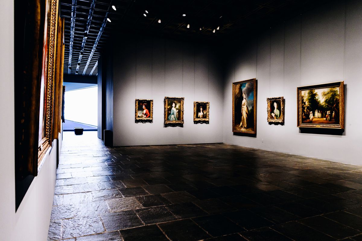 A dark gallery with paintings arranged on a wall.