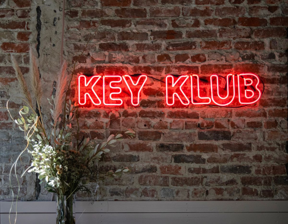 A red neon sign reading “Key Klub” on a brick wall.