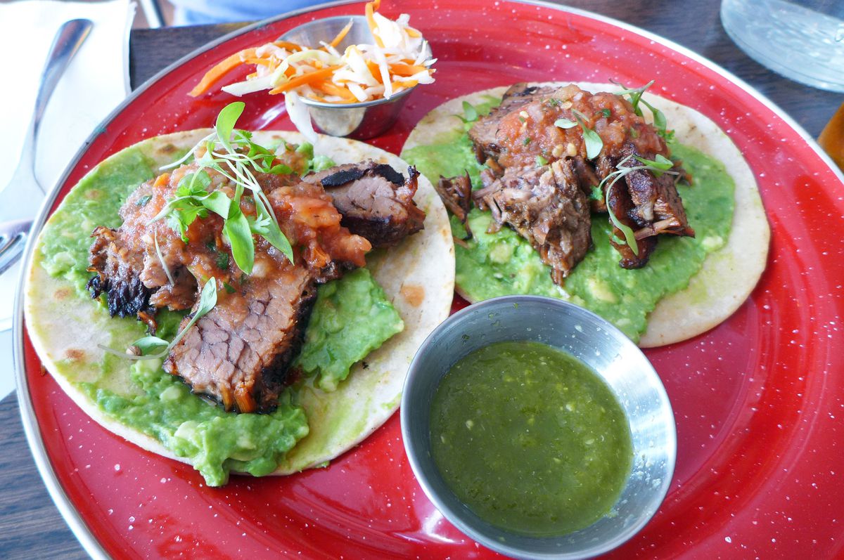 Two Guatemalan tacos are smeared with avocado and topped with slabs of beef brisket.