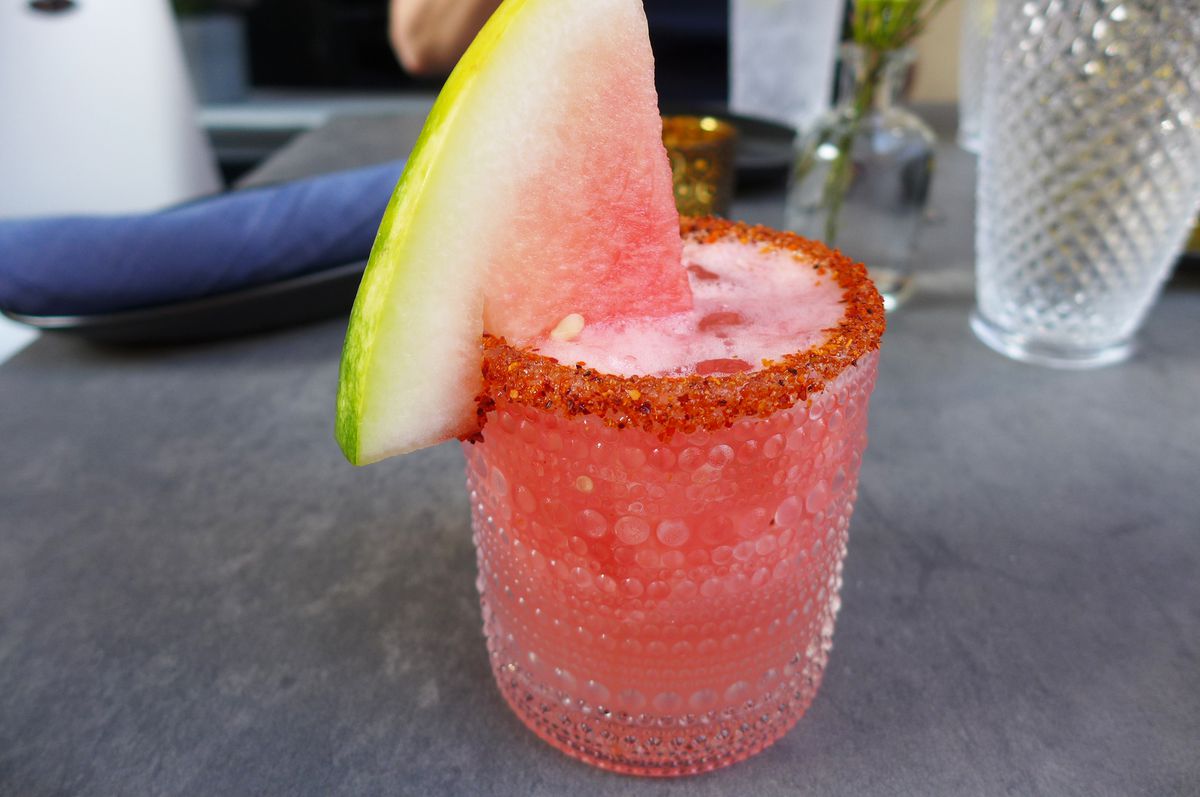 A glass with a red spice rim and slice of watermelon on the rim.