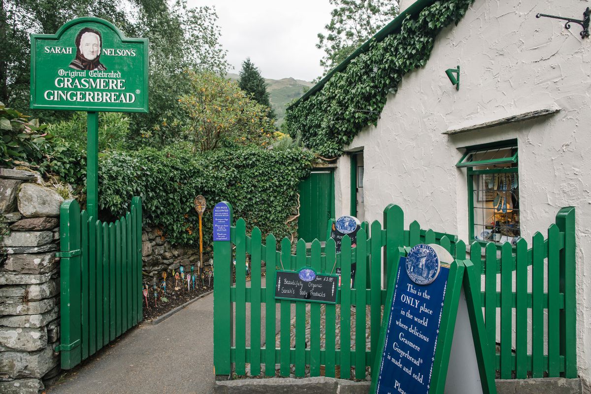 The exterior of a small, stucco-sided house, with a green picket fence, and large signs promoting Grasmere Gingerbread. 