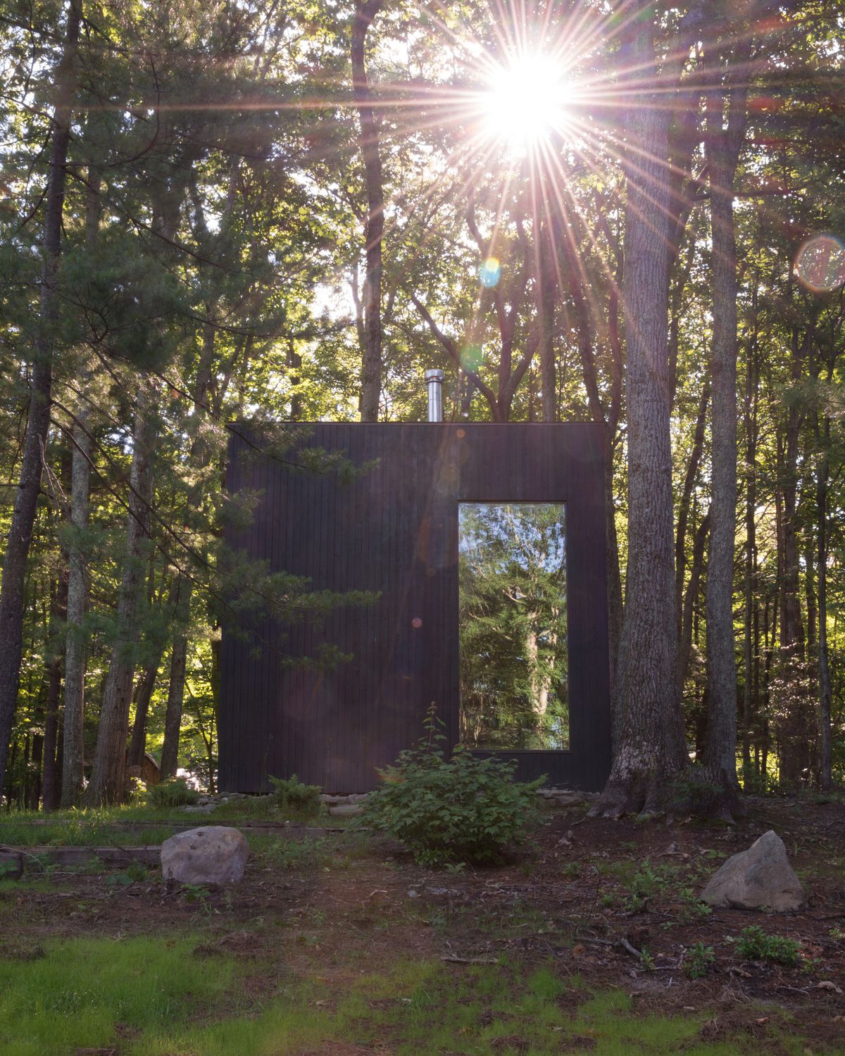 The cabin's big window mirrors the trees around it.