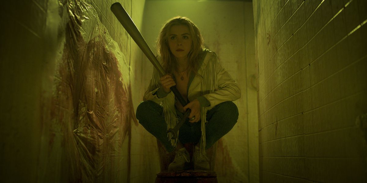 Kiernan Shipka crouches in a bathroom stall, holding a bat, as blood is splattered on the walls around her in Totally Killer.
