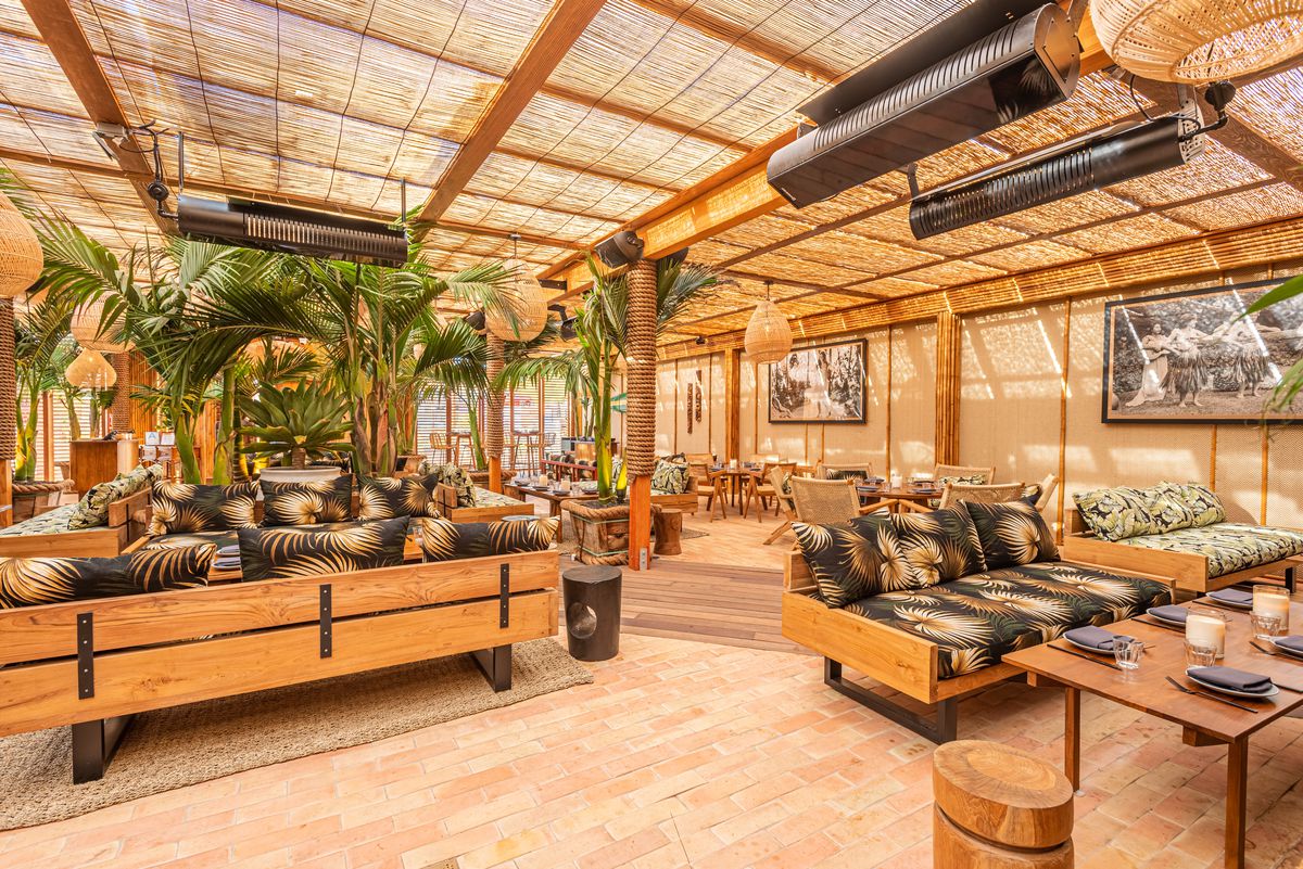 Lounge area with patterned sofas and tropical plants with heaters hanging over.