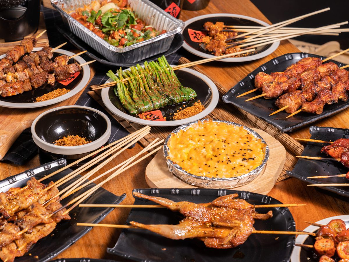 A table full of plates of various skewers, including meat, shrimp, and vegetables