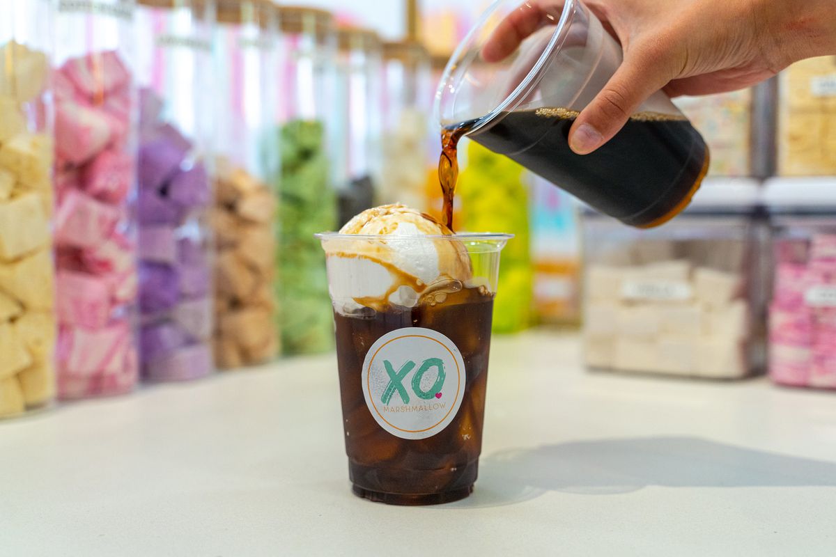 A hand pours cold brew from a plastic cup into another plastic cup that already contains a scoop of fluff and more coffee.
