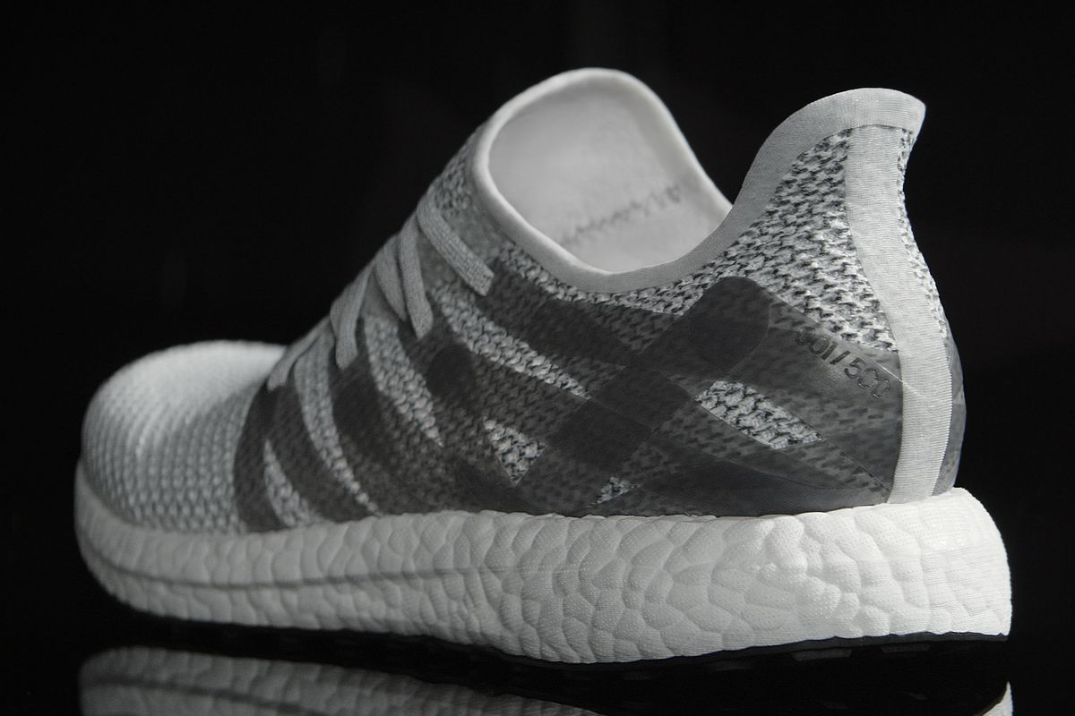 A white and grey Adidas sneaker on a black background, seen from behind. It looks almost like it's molded from a single piece of white rubber. It's a slip-on style with cross-hatched grey stripes over a smaller grey and white pattern similar to houndstoot